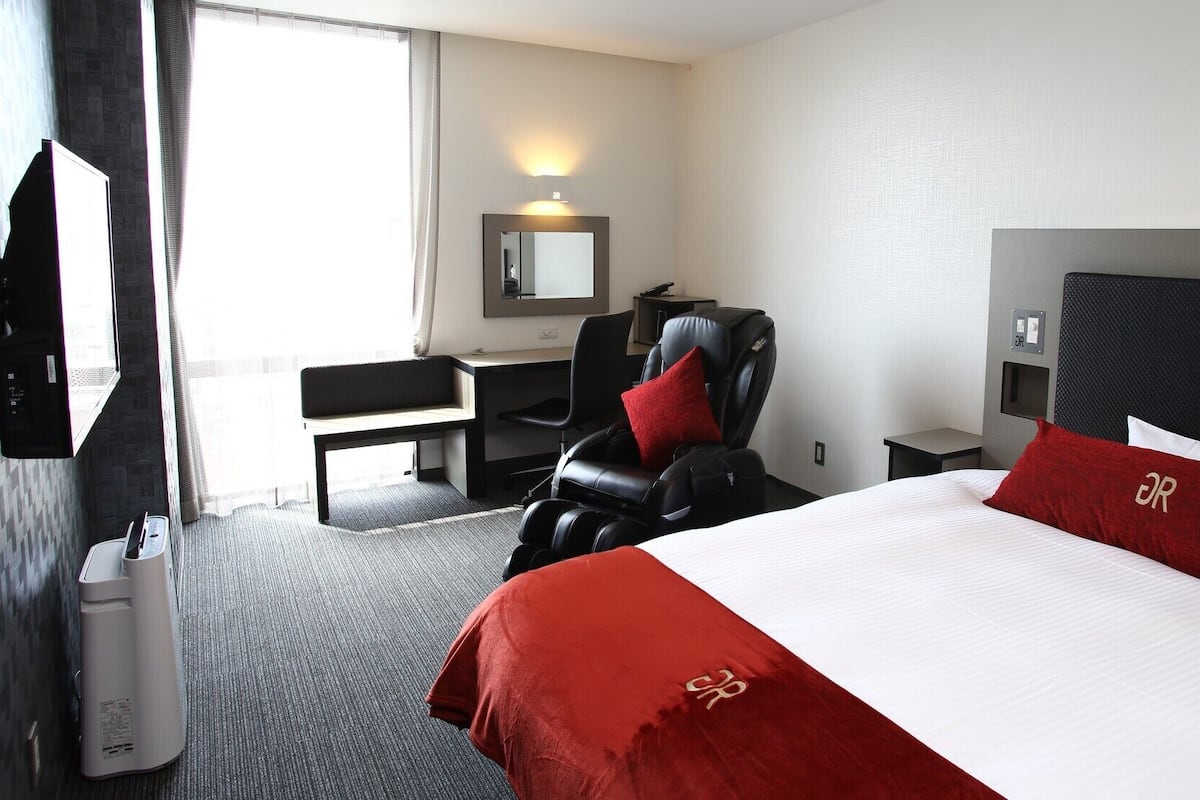Une chambre d’hôtel équipée d’un lit, d’un fauteuil massant, d’un bureau, d’une chaise, d’une télévision et d’un miroir.