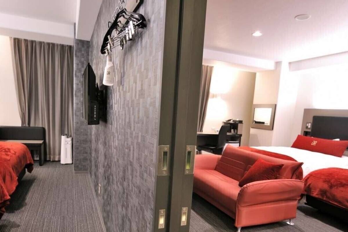A hotel room with two beds, a sofa, a desk, a TV, and a bathroom.