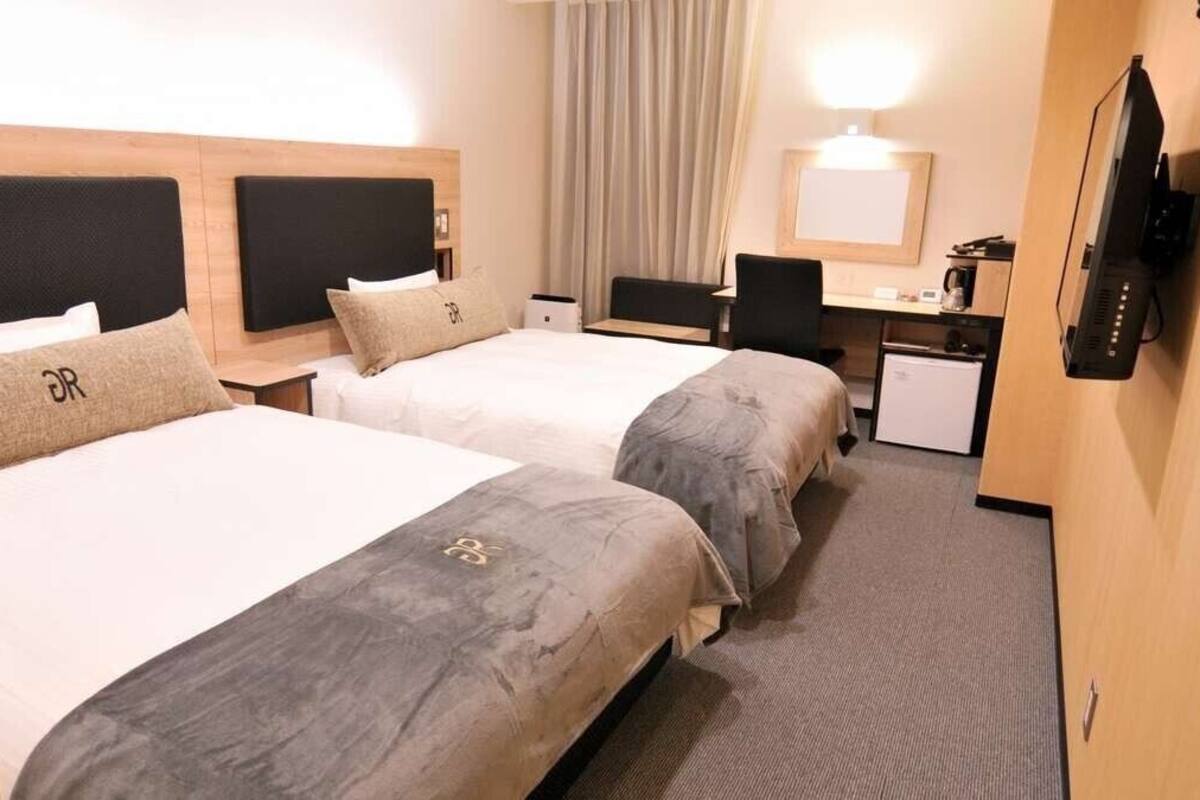 A hotel room with two beds, a desk, a television, and a small refrigerator.