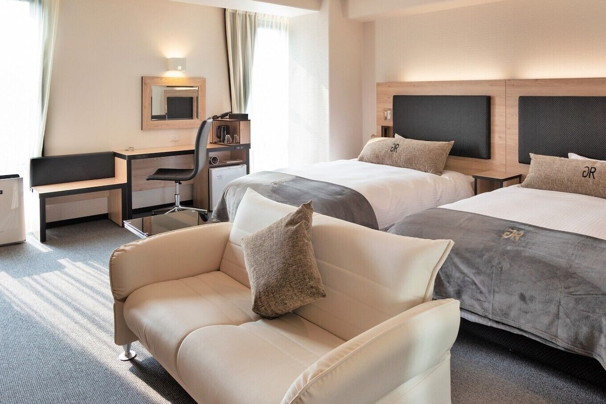 A hotel room with two beds, a desk, a chair, and a sofa.
