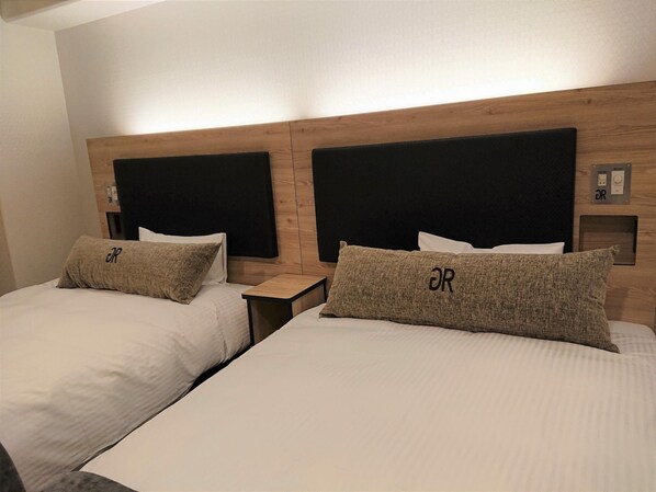 Ett hotellrum med två sängar, var och en med en sänggavel, ett sängbord och en kudde med en logotyp.