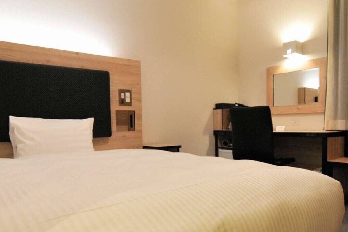 A hotel room with a large bed, a desk, a chair, a mirror, and a small shelf.