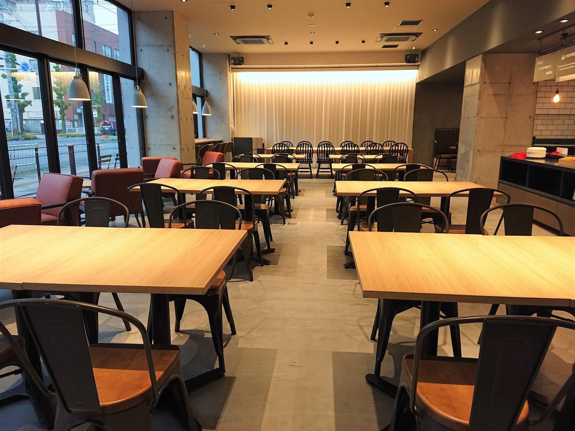 A restaurant with multiple tables and chairs, large windows, and a view of the street outside.