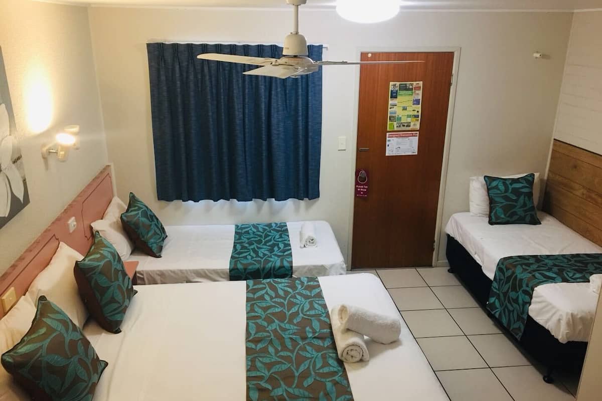 A hotel room with two single beds, a ceiling fan, a door with a bulletin board, and a tiled floor.