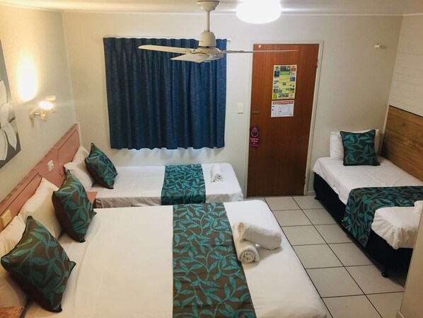A hotel room with two single beds, a ceiling fan, a door with a bulletin board, and a tiled floor.
