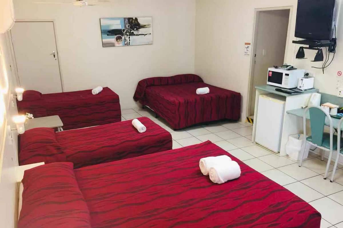 A hotel room with three beds, a desk with a computer, a television, and a microwave.
