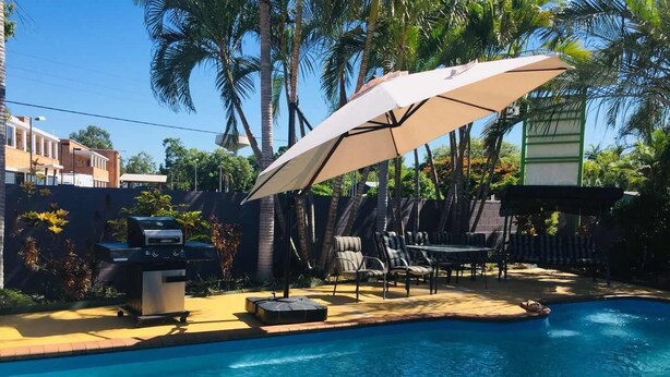 Un patio trasero con piscina, barbacoa, mobiliario exterior y palmeras.