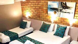 Habitación de hotel con dos camas, cada una con una colcha verde estampada y ropa de cama blanca. Se ve una pared de ladrillo y un cuadro sobre las camas.