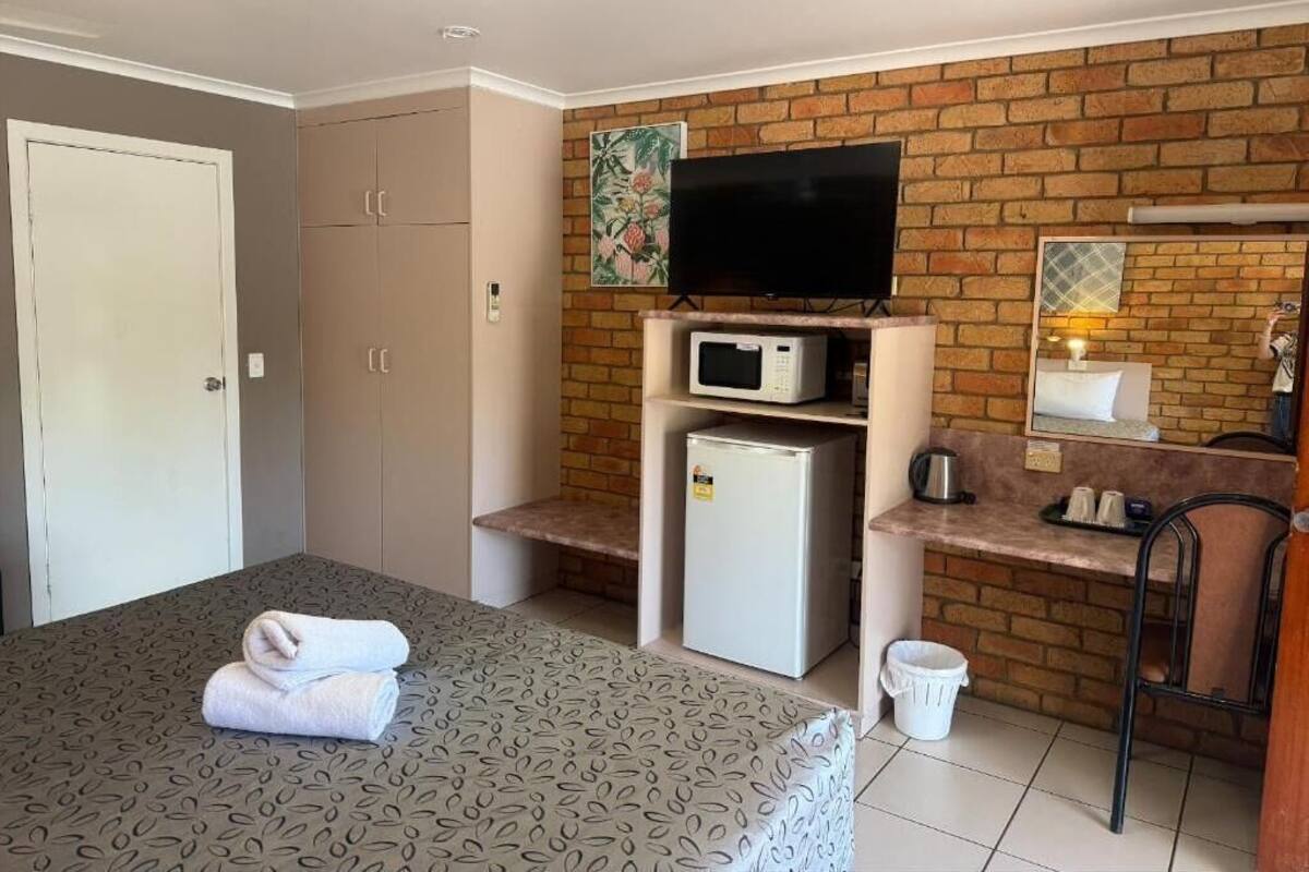A hotel room with a bed, a TV, a microwave, a refrigerator, a desk with a chair, and a bathroom.