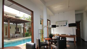 A poolside area with a wooden table and chairs, a potted plant, and a view of the pool and outdoor seating. - Chic Quarter Residence (Jakarta)