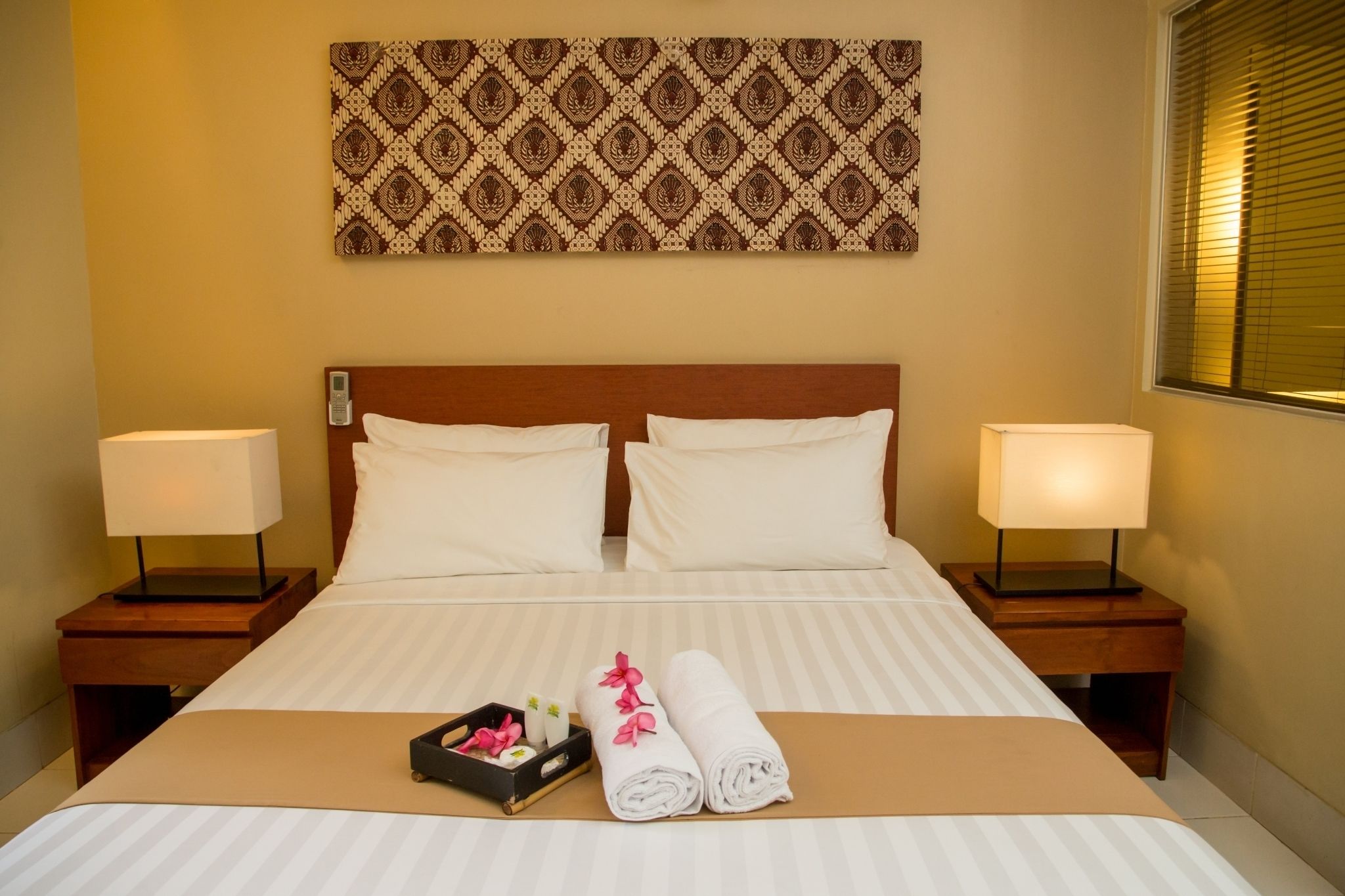 Hotelkamer met een groot bed, twee nachtkastjes met lampen, een wanddecoratie met patroon, en netjes opgevouwen handdoeken op het bed.