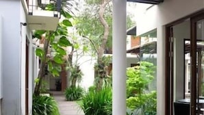 A narrow pathway flanked by lush greenery and white pillars, leading to a glass door entrance. - Chic Quarter Residence (Jakarta)