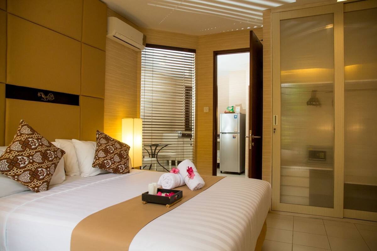 Een hotelkamer met een bed, kussens, een nachtkastje, een lamp, een koelkast en een schuifdeur.