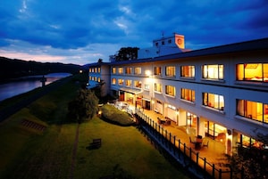 Un hotel de varios pisos con un exterior bien iluminado, una zona de estar cubierta al aire libre y vistas a un río.