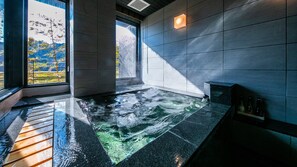 A spa room with a hot tub, a window with a view of trees, and a wall-mounted light fixture. - Suiranrou (Hitoyoshi)