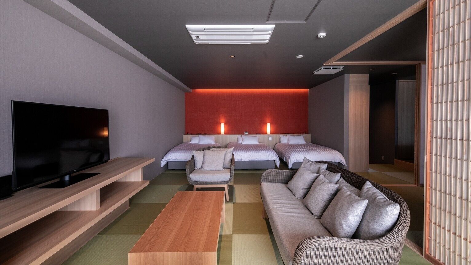 A modern hotel room with a flat-screen TV, two beds, a sofa, a coffee table, and a wall-mounted TV.
