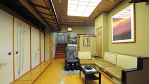 Ein traditionelles japanisches Interieur mit Tatami-Böden, einem niedrigen Tisch, einer Couch und einer Treppe, die in einen anderen Raum führt.