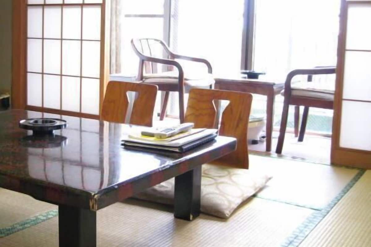 A traditional Japanese room with tatami flooring, a low wooden table, and two tatami mats with chairs.
