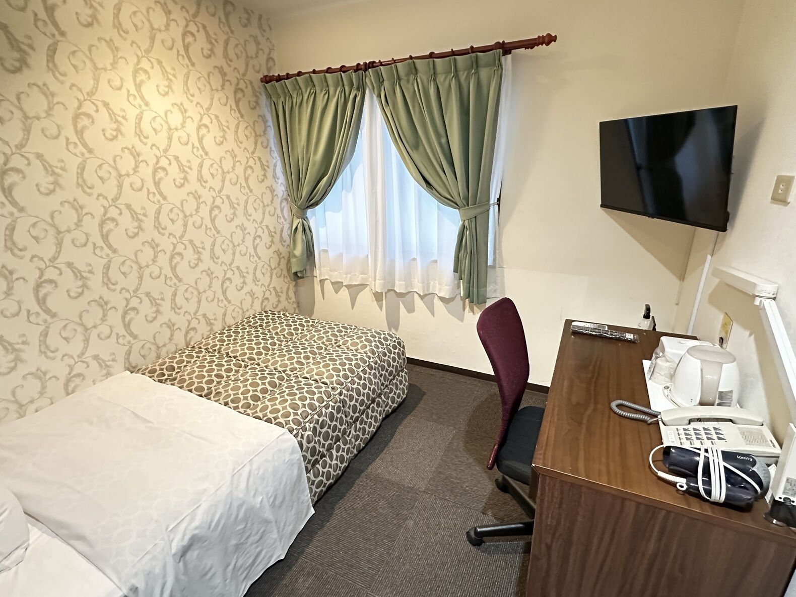 Een hotelkamer met een bed, een bureau met telefoon en koffiezetapparaat, een stoel en een televisie aan de muur.