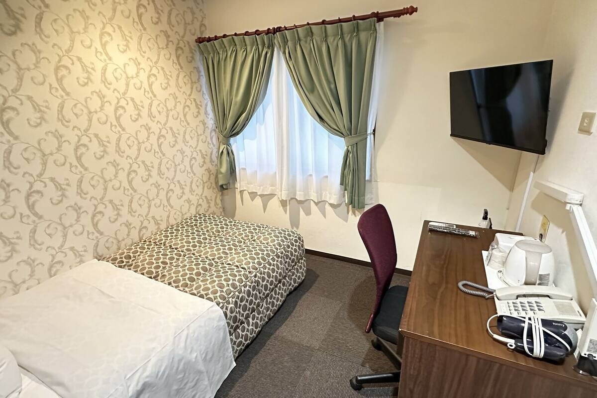 Een hotelkamer met een bed, een bureau met telefoon en koffiezetapparaat, een stoel en een televisie aan de muur.