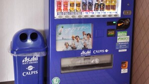 A blue vending machine with multiple beverage options, including soft drinks and snacks, next to a blue trash bin. - Futsukaichi Green Hotel (Chikushino)