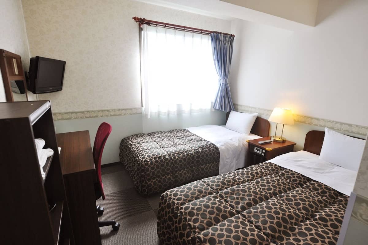 Een hotelkamer met twee bedden, een bureau met stoel, een televisie en een raam met gordijnen.