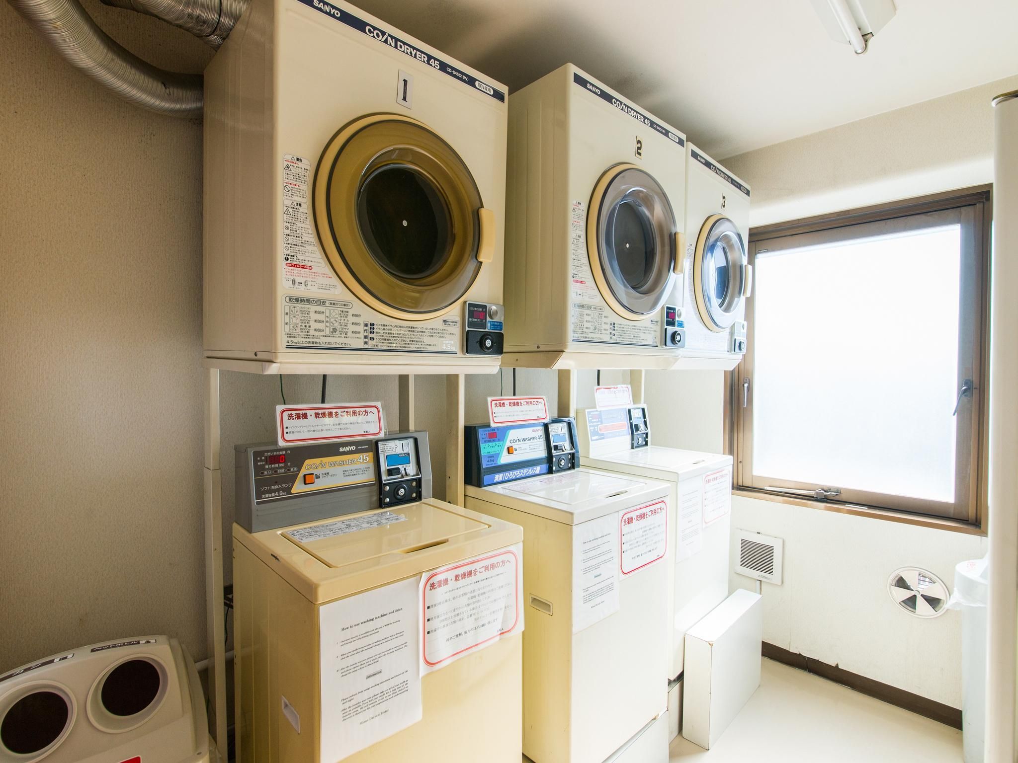 A laundry facility with two stacked washing machines and a dryer, each with a control panel and safety instructions.