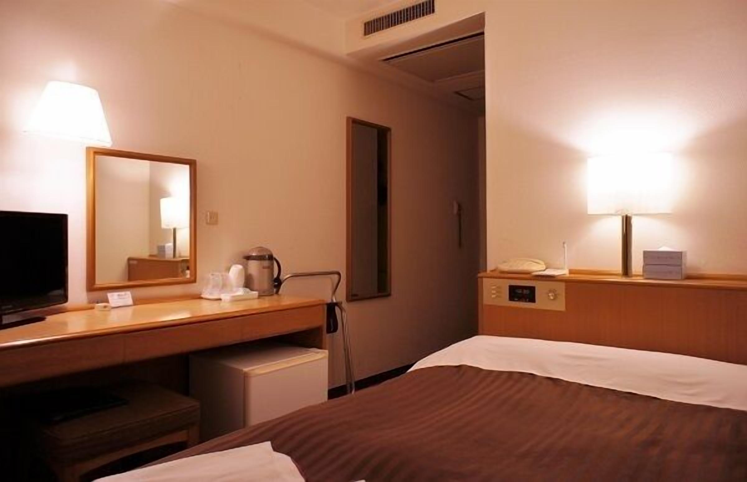 Ein Hotelzimmer mit einem Bett, einem Schreibtisch mit Lampe, einem Fernseher und einem Spiegel.