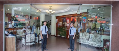 The entrance of a hotel with a reception area, a sushi restaurant, and a seating area with patterned chairs.