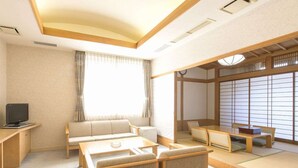 Una tradizionale stanza in stile giapponese, con pavimento in tatami, un tavolino con cuscini, una poltrona e un televisore su un supporto in legno.