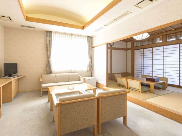 A traditional Japanese-style room with tatami flooring, a low table with cushions, a sofa, and a television on a wooden stand.