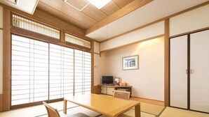 Una tradizionale stanza giapponese con pavimento in tatami, un tavolino basso, una panca imbottita, porte scorrevoli, un televisore e un quadro appeso al muro.