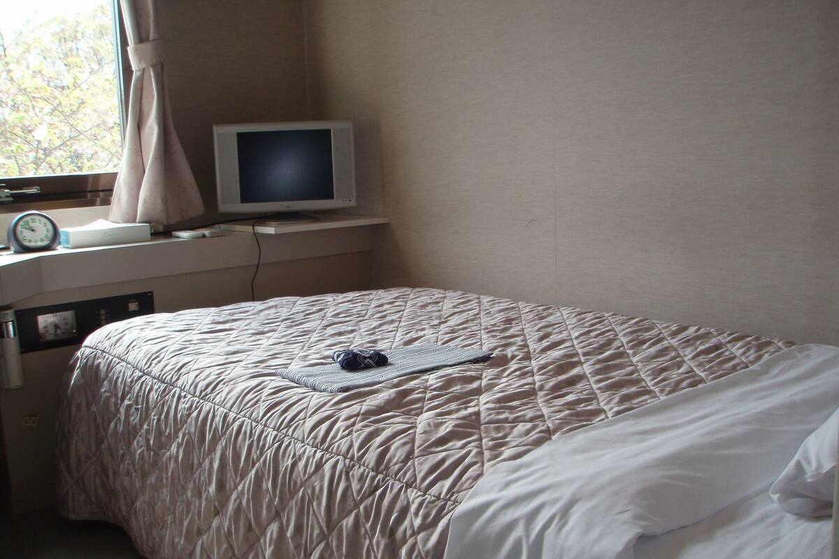 A bedroom with a bed, a television on a stand, a clock, and a thermostat.