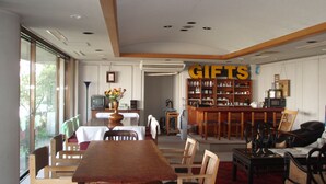 A dining area with a wooden table and chairs, a bar area with shelves labeled 'GIFTS', and a view through a glass door. - Jyonai Hotel (Karatsu)