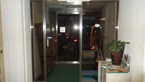 A hotel entrance with a glass door, a green mat, a reception desk, and a potted plant. - Jyonai Hotel (Karatsu)