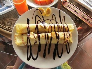 A plate of crepes with chocolate sauce and banana slices on a table. - Kampung Cenik (Legian)