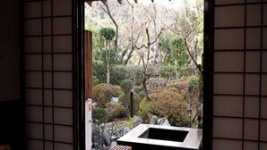 A traditional Japanese interior with tatami flooring, a low table, and a view of a garden with a water feature. - Ryokan Satsumanosato (Satsumasendai)