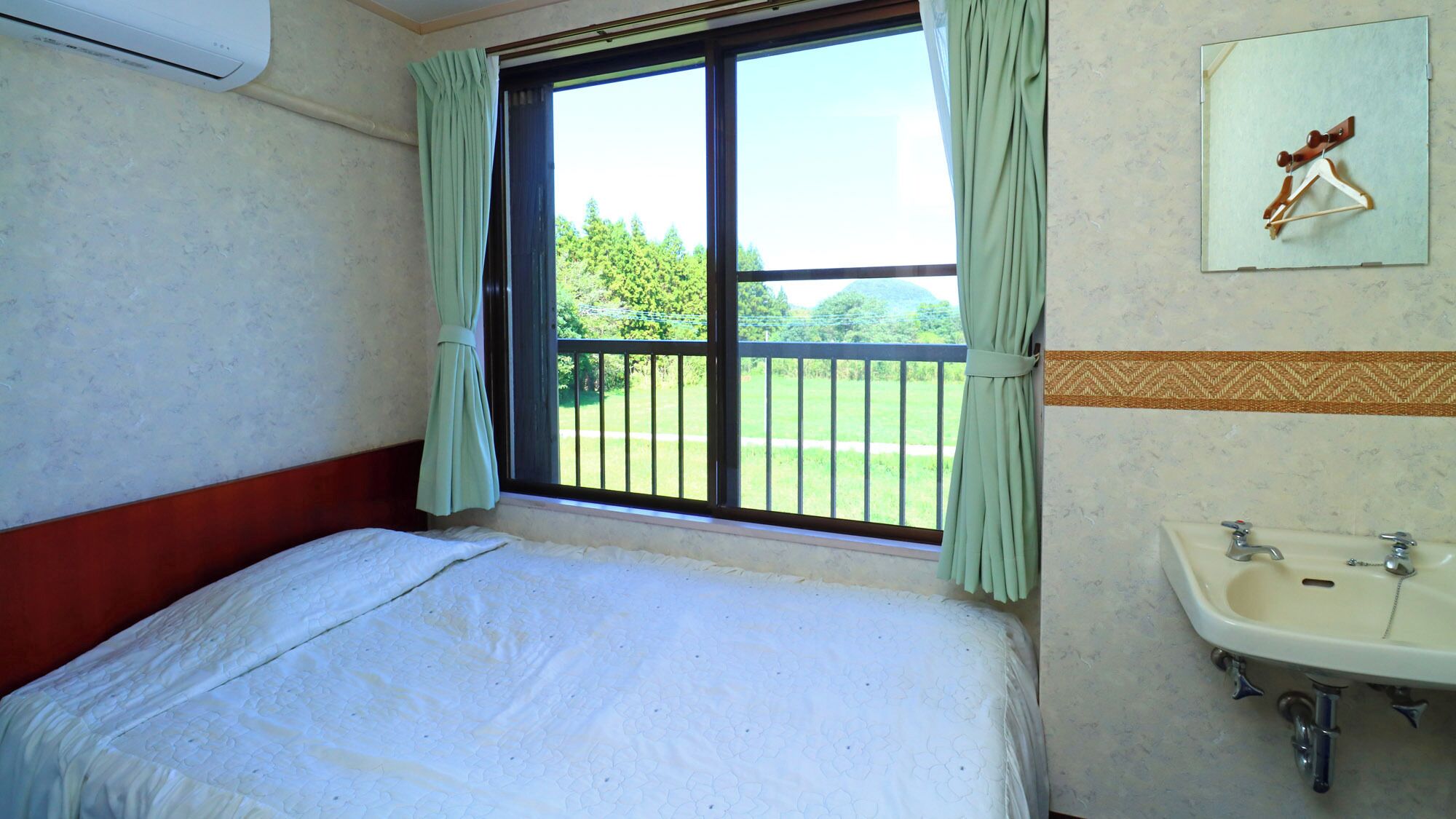 A room with a bed, a window with curtains, a balcony, and a bathroom with a sink.