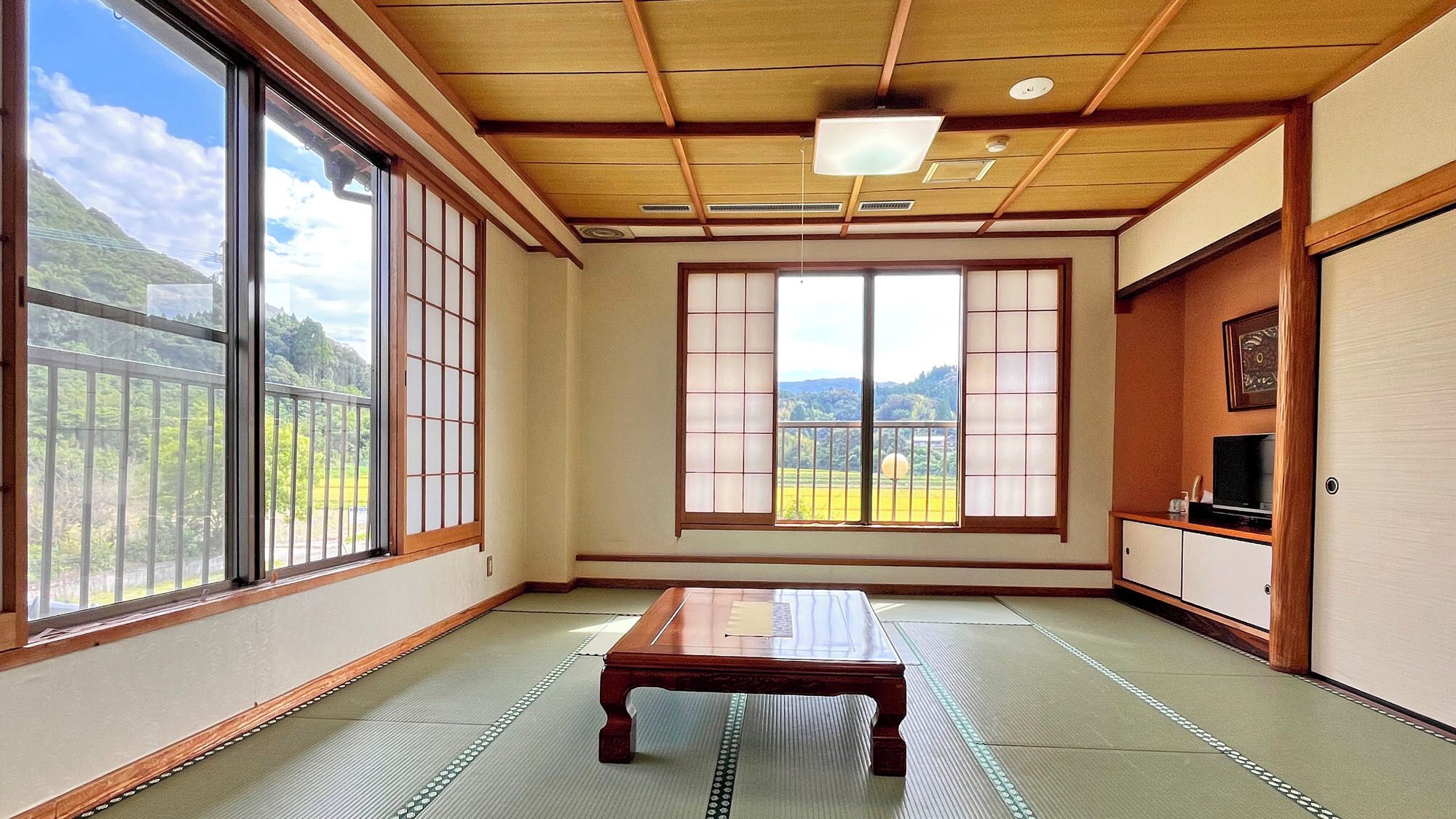 A traditional Japanese room with tatami flooring, sliding shoji doors, a tatami mat table, and a television on a wooden cabinet.