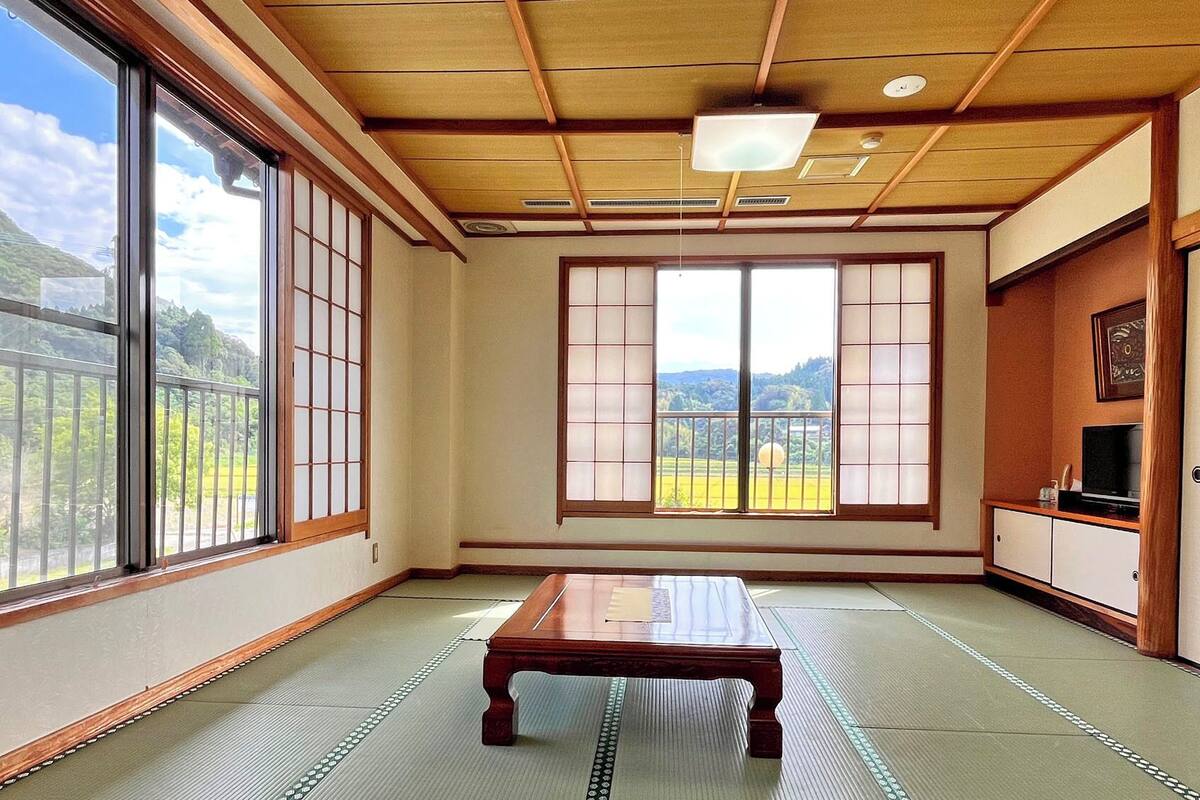 Een traditionele Japanse kamer met tatami vloerbedekking, verschuifbare shoji deuren, een laag tafeltje van tatami en een televisie op een houten kast.