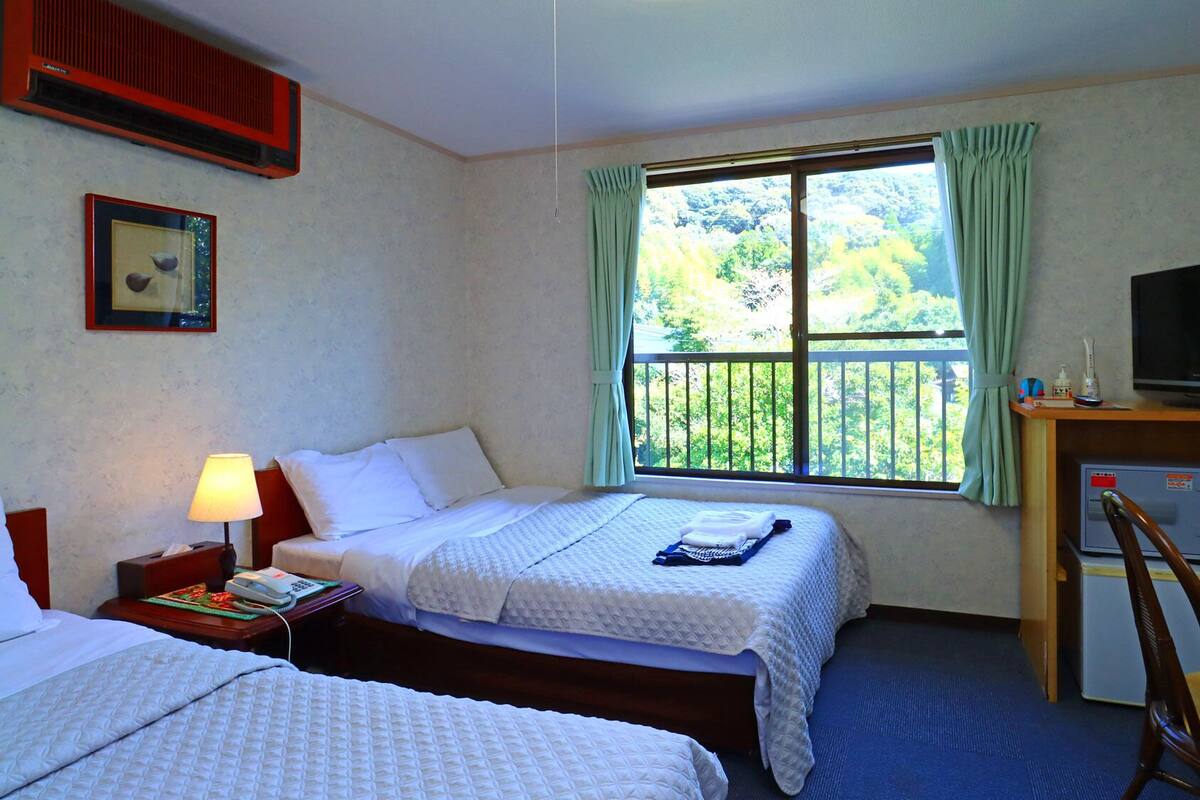 Een hotelkamer met twee bedden, een televisie, een bureau met stoel, een raam met gordijnen en een airconditioning.
