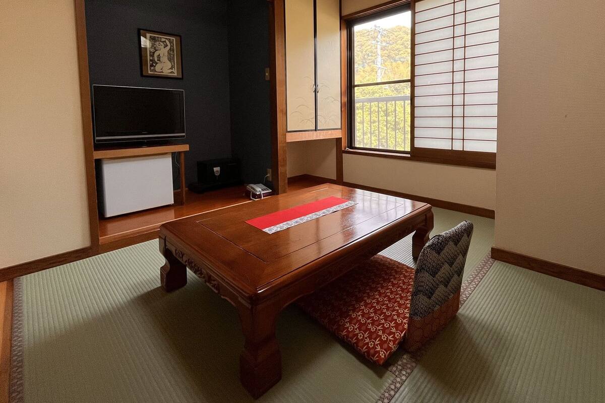 Een traditionele Japanse kamer met tatami vloeren, een lage houten tafel, een kussenbank, een schuifdeur en uitzicht door een shoji scherm.