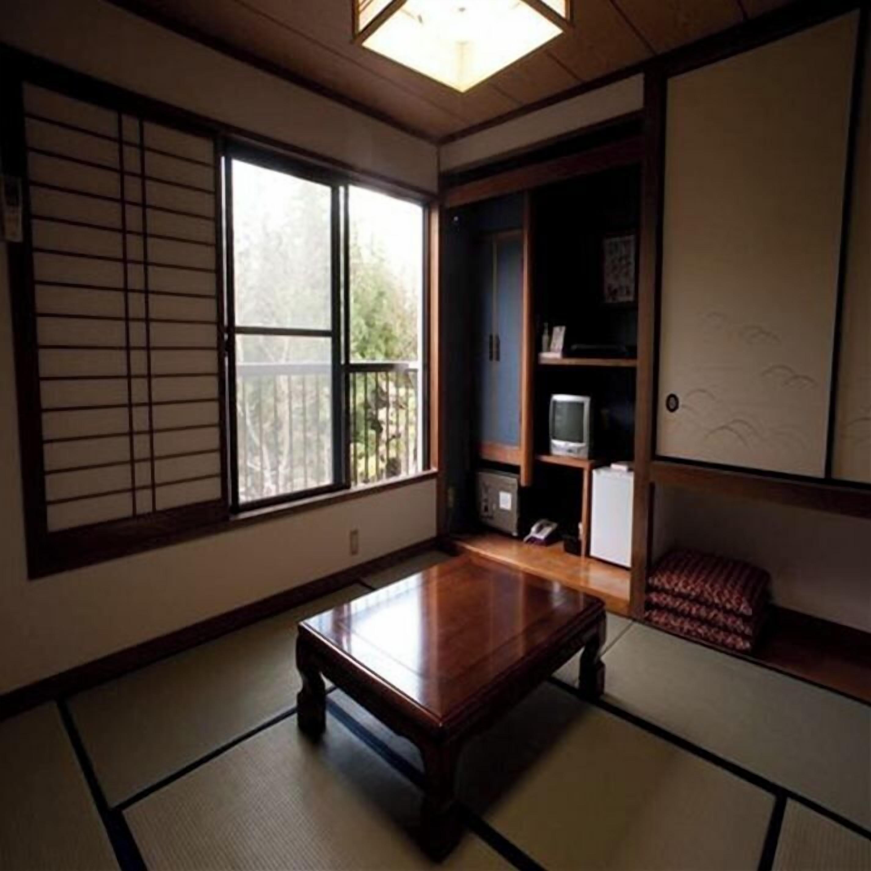 A traditional Japanese room with tatami flooring, a low wooden table, a sliding door, and a television on a shelf.