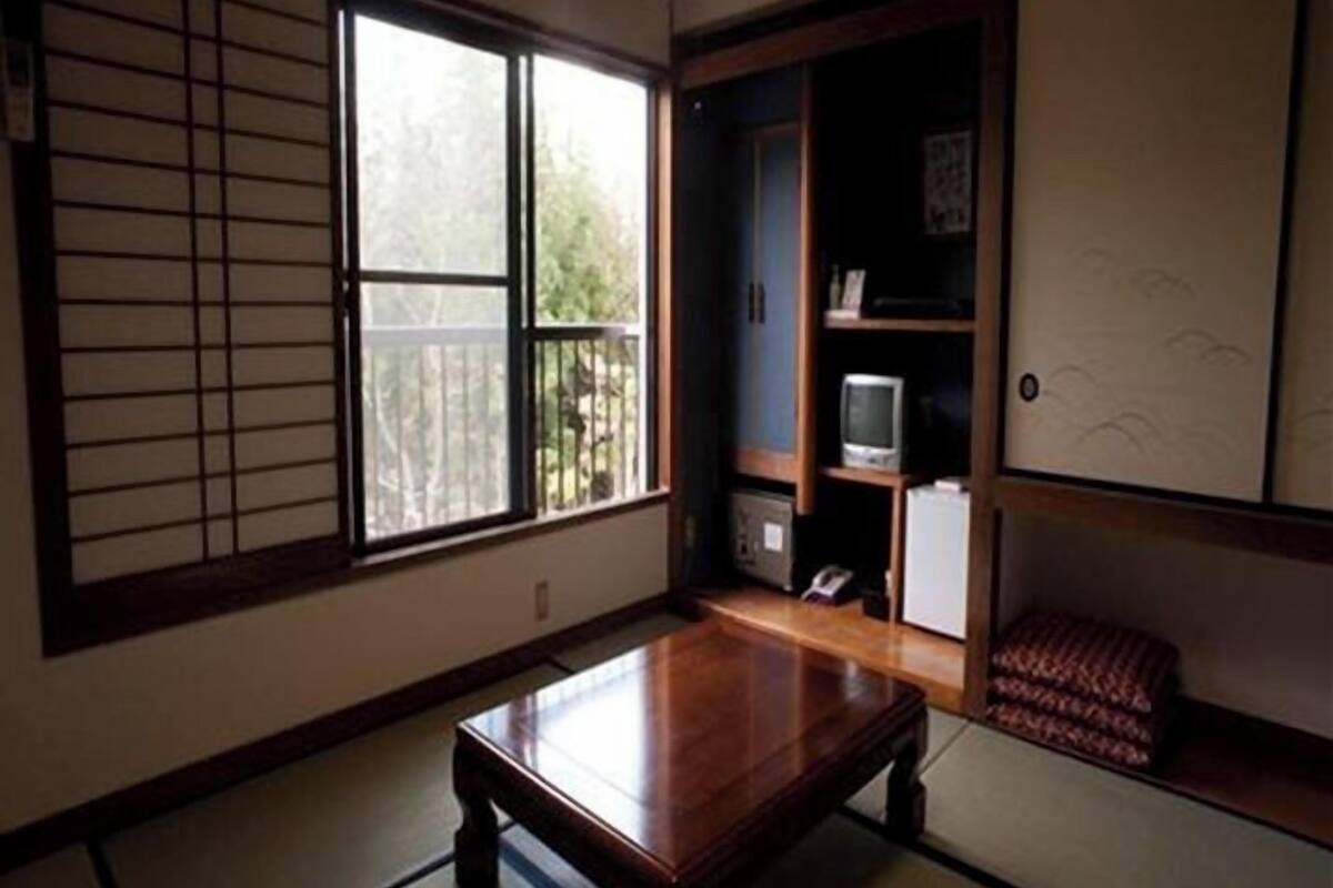 Een traditionele Japanse kamer met tatami vloerbedekking, een lage houten tafel, een schuifdeur en een televisie op een plank.