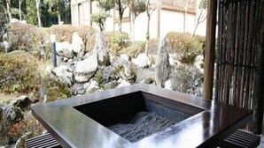 A rectangular stone hot tub with a dark surface, surrounded by wooden benches and a stone pathway. - Ryokan Satsumanosato (Satsumasendai)