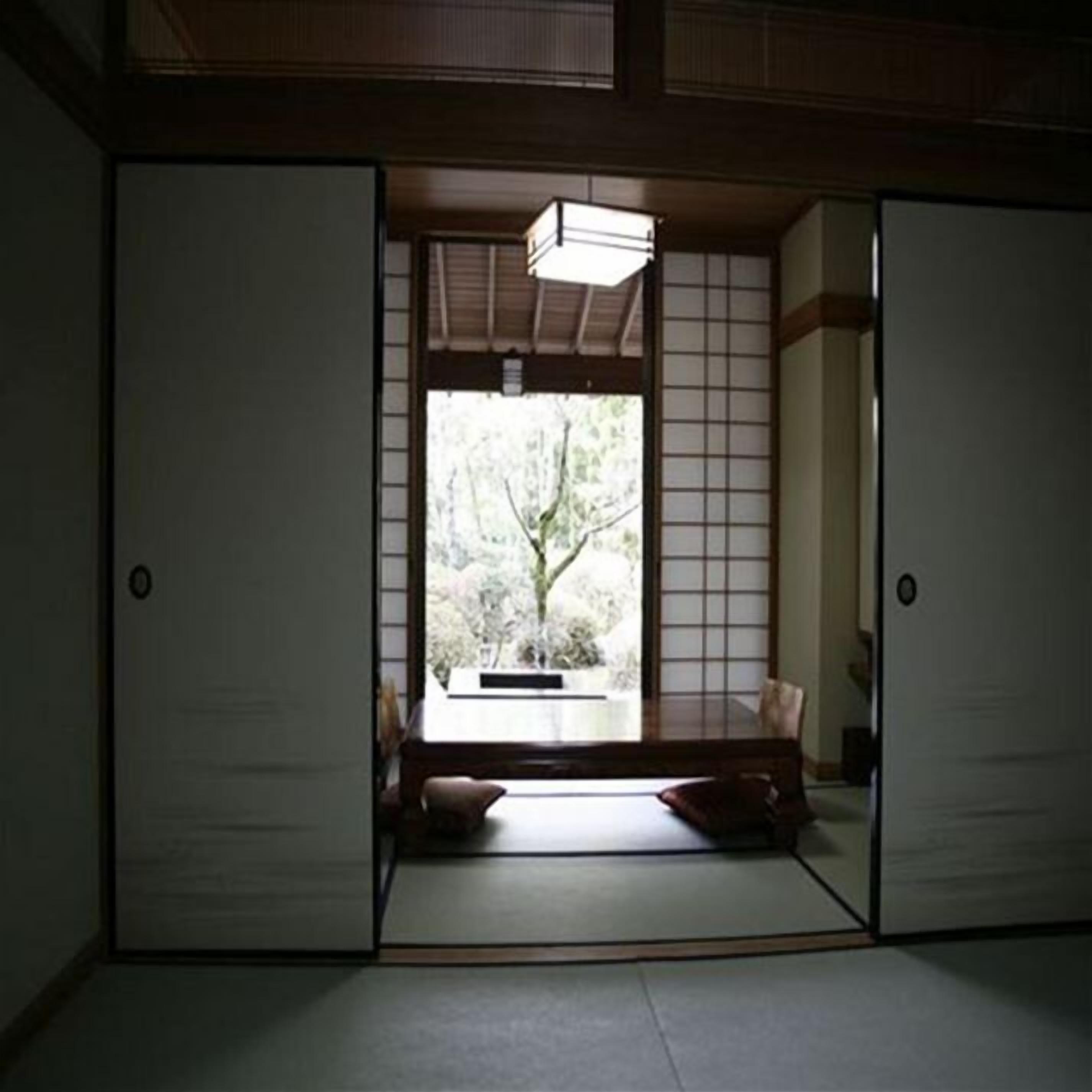 A traditional Japanese room with tatami flooring, sliding doors, and a view of greenery outside.