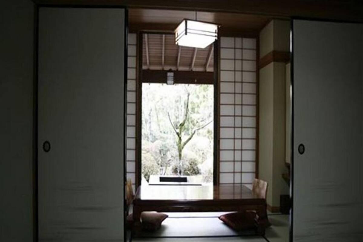 Een traditionele Japanse kamer met tatami vloeren, schuifdeuren en uitzicht op groen.