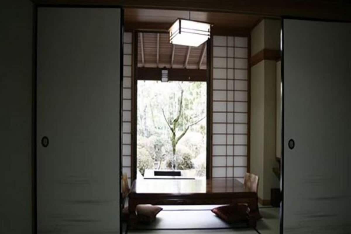 A traditional Japanese room with tatami flooring, sliding doors, and a view of greenery outside.