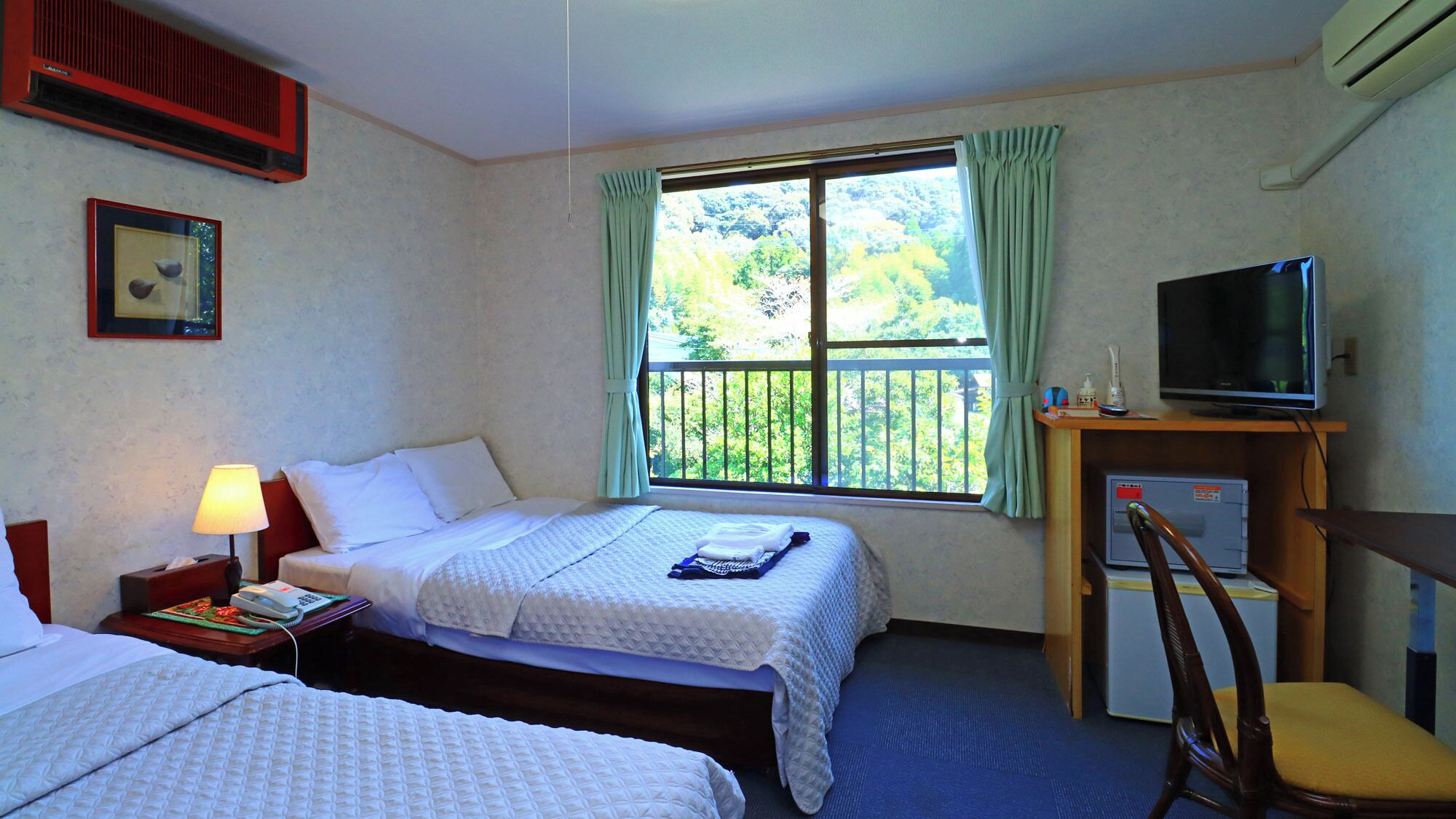 A hotel room with two beds, a desk with a television, a chair, and a window with curtains.