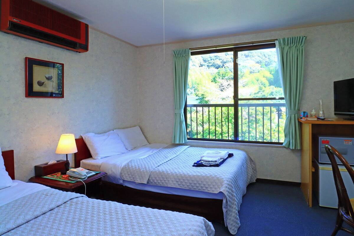 Een hotelkamer met twee bedden, een bureau met televisie, een stoel en een raam met gordijnen.